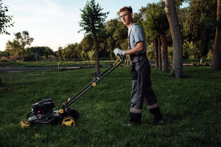 A young male gardener in overalls uses a lawn mower.Man mows the lawn with a lawn mower.Gardening...