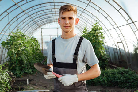 Man with garden tools.Young happy farmer posing with abrasive tools in a greenhouse.Man posing with garden tools.Gardening, Farming and Agriculture Conceptの写真素材