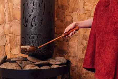 Woman hand pouring water into hot stone in the wooden traditional sauna spa room.の写真素材