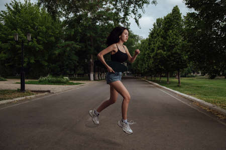 Young girl jumping with a skateboard in the city.young girl in a black tank top and blue shorts posing with a skateboard.Concept of youth recreation, lifestyle. Skateboarder in the city.の写真素材