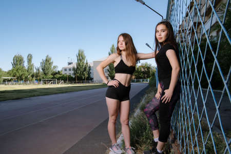 Two girls in sportswear posing at the stadium.Portrait of two sports girlfriends at the sports stadium.Sport and healthy lifestyle.の写真素材