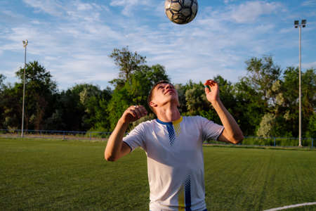 Young male soccer player juggles a ball on a soccer field.sport, football and people - soccer player playing and juggling ball using header technique on field.Football sports conceptの写真素材
