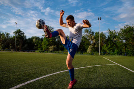 Young male soccer player juggles a ball on a soccer field.Athlete juggling the football with his feet in stadium.Football sports conceptの写真素材