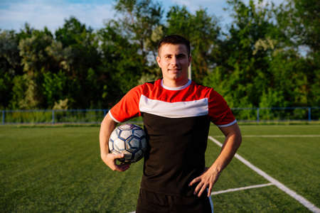 Soccer player with a ball in his hands.Portrait of a young football player holding a football ball in his hands on a football field.Football sports conceptの写真素材