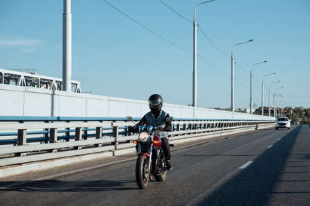 Man rides a motorcycle in the city.Young man in helmet and equipment rides a motorcycle on the road.Motorcyclist riding a bike during the day on the roadの写真素材