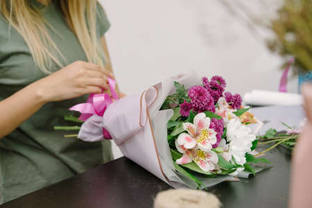 Florist at work: pretty young woman making fashion modern bouquet of different flowers. Florist woman creates flower. Floral shop concept. Handsome fresh bunch.