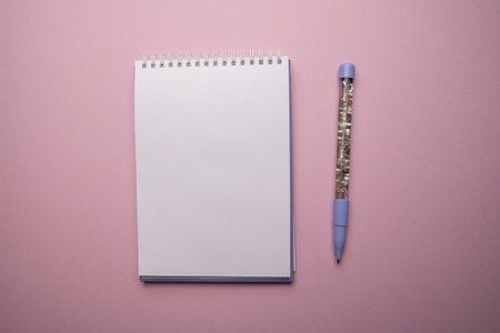 Top view of open empty spiral notebook with pen on pink background, flat lay