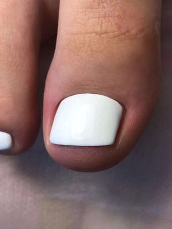 White pedicure. Whitepedicure on female feet.Woman feet with White pedicure on gray background