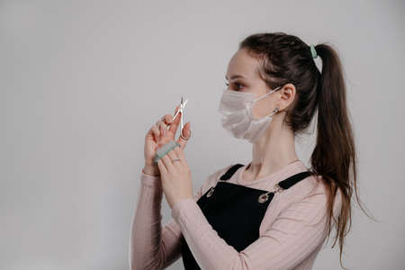 Manicure tools in hands of female manicurist wearing mask. woman brunette manicurist on gray...