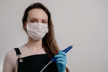 Manicure tools in hands of female manicurist wearing mask and gloves. woman brunette manicurist on...