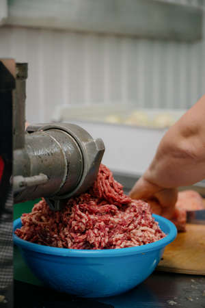 raw meat. The process of preparing forcemeat by means of a meat grinder.Side view of a meat grinder...