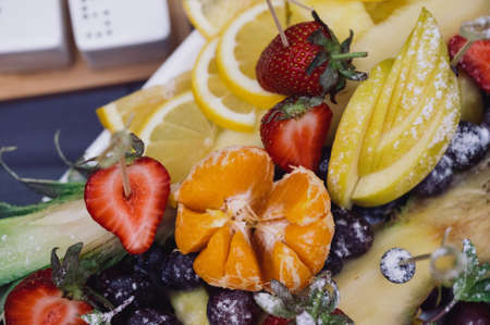 Raw fruits berries assortment platter on the white plate, on the off white table, selective focus.Sliced fruits on a plate on the tableの写真素材