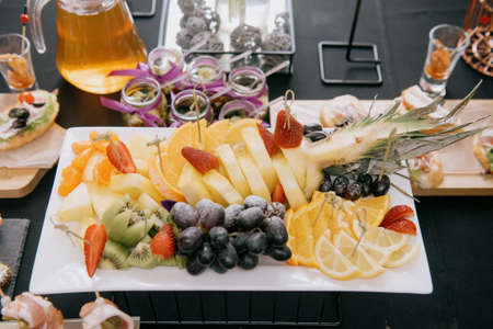 Raw fruits berries assortment platter on the white plate, on the off white table, selective focus.Sliced fruits on a plate on the tableの写真素材