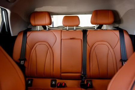 Interior view of a luxury car showcasing brown leather seats with black seat belts, silver headrests, and a black center console with various controls.の写真素材
