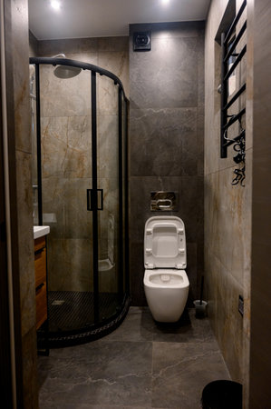 Modern interior of bathroom in luxury apartment. Gray marble tile. White sink and toilet. Shower...