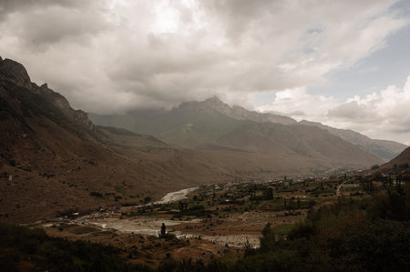 Panoramic view of a mountain valley with a village and a river flowing through it.a wide valley between brown mountains, with a village and a bed river in the center.の写真素材