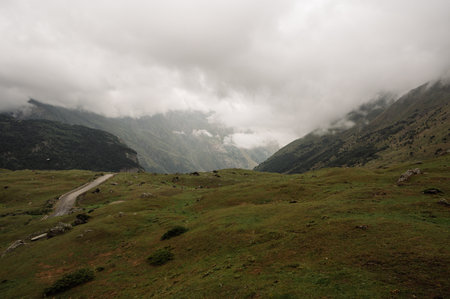 View of a misty valley in the mountains through grassy hills.A country road leads deep into a...
