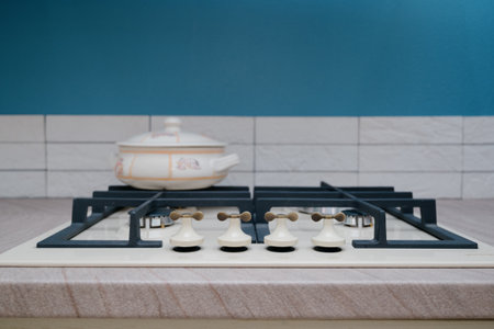 Close-up of a beige gas cooktop with a cast iron grate and a ceramic pot. A modern kitchen stove with unusual handles and a light-colored saucepan on the countertop.の写真素材