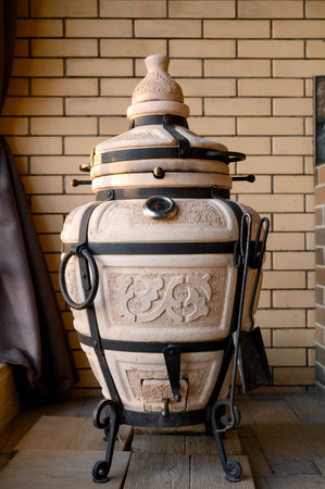 A large ceramic tandoor with a thermometer, forged legs and accessories on the terrace. Traditional clay tandoor oven with decorative ornamentation and black metal frame.の写真素材