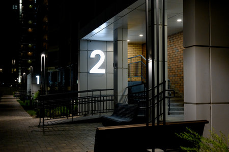 Street entrance to an apartment building with landscaping elements. A luminous number above the entrance to a modern residential complex at night.の写真素材