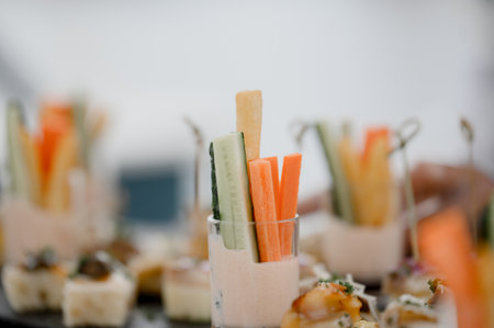 Close-up of a glass with carrot and cucumber vegetable sticks with sauce on a buffet table. Light snacks vegetarian sticks made of fresh vegetables on a trayの写真素材