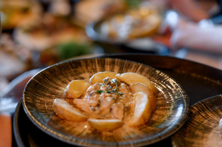 A serving of fried potatoes and creamy julienne with mushrooms and chicken. A delicious dish with chunks of potato and a thick sauce on a black plate.の写真素材