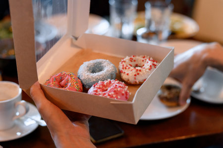 A hand holds a box with four colorful glazed donuts. Close-up of a box of pink, white and blue donuts in a customer's hand.の写真素材