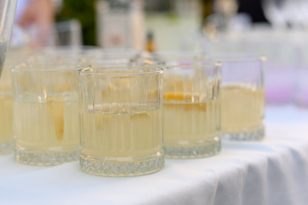 A row of glasses with lemonade or cocktail on a white tablecloth. Close-up of refreshing drinks with citrus fruits on the table for guests at the event.の写真素材