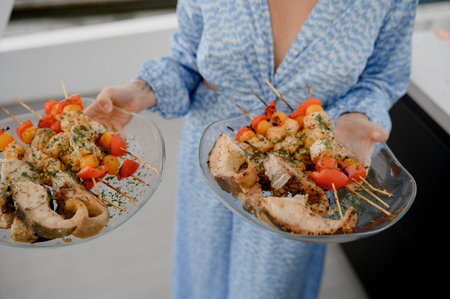 Baked fish steaks and vegetable kebabs with herbs on two transparent plates in hands.の写真素材