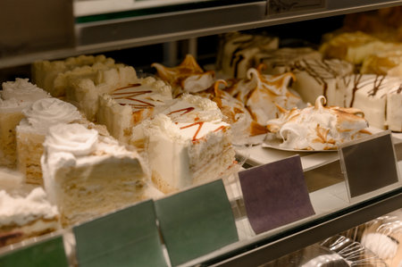 Rows of cakes and pieces of cream cake on a shelf in a pastry shop display case. A variety of sweet desserts with cream and icing for sale in a pastry shop.の写真素材