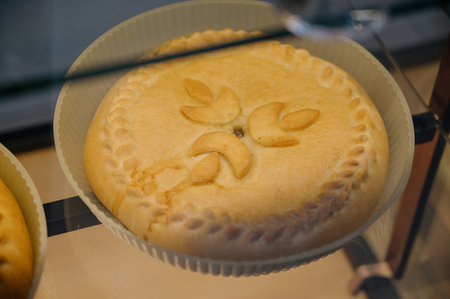 A close-up of a round, golden-brown pie with pastry decoration.Traditional Russian pie with a golden...