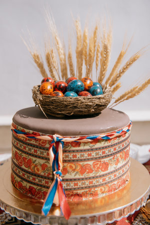 A festive cake decorated with a nest of brightly colored quail Easter eggs. An original Easter or spring cake with an artificial nest and wheat earsの写真素材