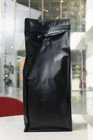 Vertical black matte coffee bag with flap on cafe table. Sealed doypack packaging with coffee against the background of blurred garland lightsの写真素材
