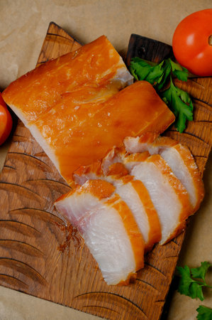Sliced hot smoked fish fillet with a golden crust on a board. Pieces of white smoked fish with herbs...