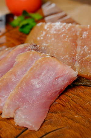Sliced smoked or dried fish fillet on a wooden board with tomatoes. Close-up of sliced cold smoked...