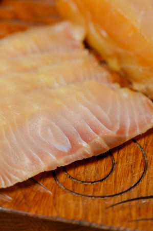 Sliced smoked or dried fish fillet on a wooden board with tomatoes. Close-up of sliced cold smoked...