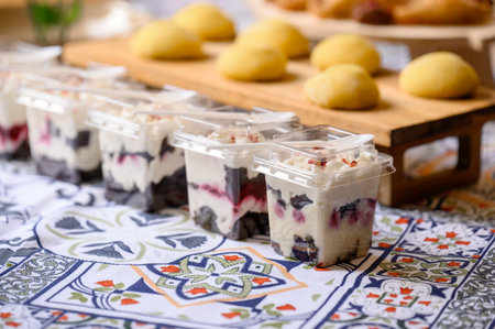 Portioned desserts with berries and cream in plastic cups on a patterned tablecloth at a buffet...