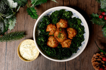 Crispy breaded meatballs with a side of greens and gravy. Golden fried croquettes on a bed of kale in a white bowl with garlic sauceの写真素材