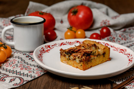 Homemade baked goods with nuts and a mug of hot drink. A slice of vegetable pie with almond petals on a plate next to an enamel mug of brothの写真素材