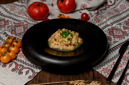 Vegetable tartare with green onions in a black deep plate. Appetizer of finely chopped vegetables in a black ceramic bowl on a wooden tableの写真素材