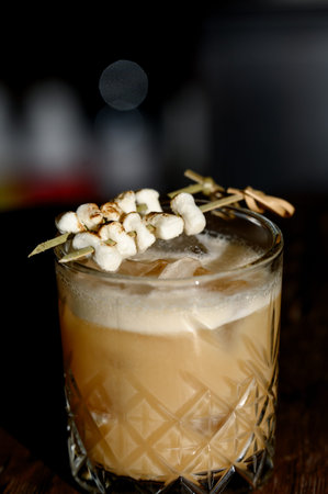 A creamy cocktail with foam and toasted marshmallows on a skewer in a rocks glass. A serving of cold...