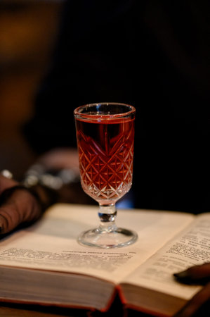 a glass of red liqueur stands on an open paper book. A glass with a bright alcoholic drink on...