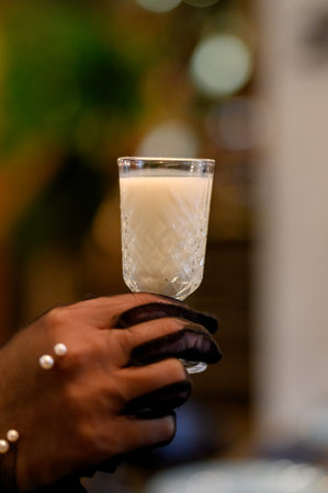 A woman's hand in a black glove holds a glass of white cream liqueur. Close-up of a hand holding a...