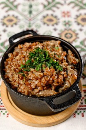 A serving of buckwheat with stewed meat in a portioned saucepan. Hot buckwheat porridge with beef and parsley in a cast iron panの写真素材