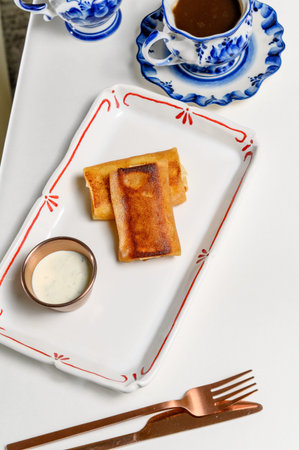 Fried pancakes with sour cream in a gravy boat and a cup of black coffee by the bed in a hotel....