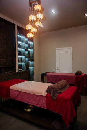 A cozy treatment room in an oriental style with ethnic decor and professional couches. Massage tables covered with red towels in a room with a decorative niche and lightingの写真素材