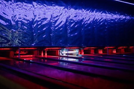 Bowling lanes with pins at the end under bright blue and pink neon lighting. A perspective view of...
