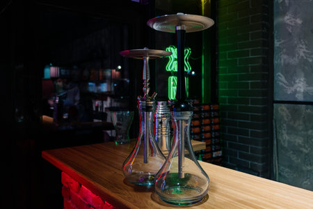Two modern glass hookahs on a wooden stand in a dark interior with neon lighting.Professional hookahs assembled against a brick wall and green neon in a nightclubの写真素材