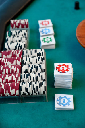 Various stacks of poker chips in red, black, and white alongside playing cards on a green felt...