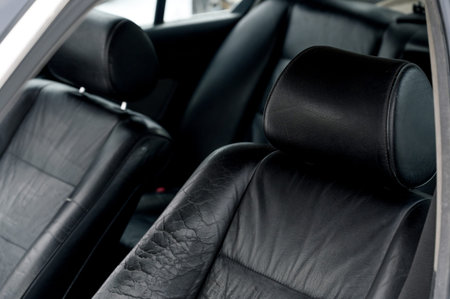 Close-up view of black leather car seats featuring headrests, showcasing wear and texture inside a vehicle's interior spaceの写真素材